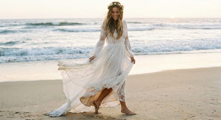 Bride in lightweight beach wedding dress walking along the ocean shore.